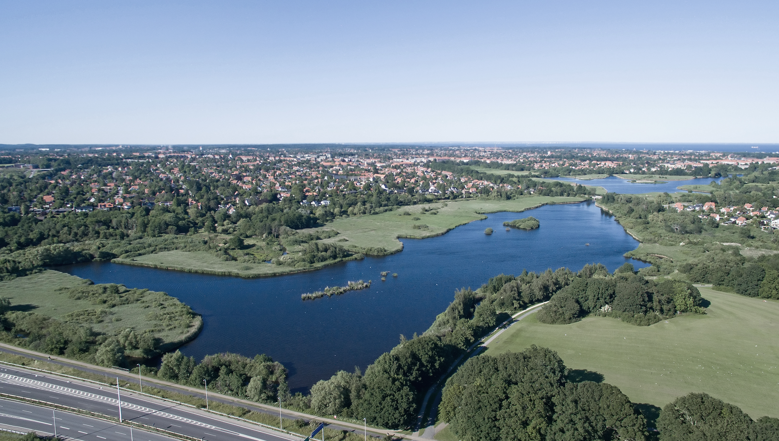 luftfoto af sø, motorvej og boliger